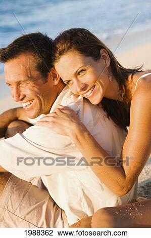 Stock Image - Hawaii, Oahu, North Shore, Happy Sit Embracing On Beach In Warm Afternoon Light.. Fotosearch