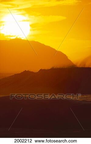 Stock Image - Hawaii, Oahu, North Shore, Large Golden Sun Ball Glowing In Orange Sky, Big Wave With Spray Backlit. Fotosearch
