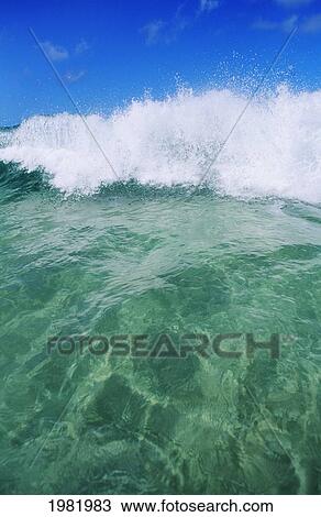 Stock Image - Hawaii, Oahu, North Shore, Small wave breaking, blue sky. Fotosearch