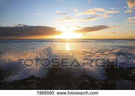 Stock Image - Hawaii, Oahu, Ocean Rushing Over Reef Rocks As A Beautiful Sunsets Behind. Fotosearch