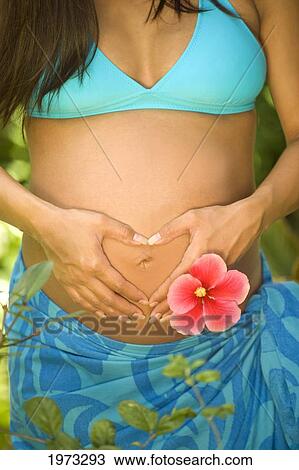 Stock Image - Hawaii, Oahu, Pregnant Girl Wearing Blue Bikini And Pero; Hands In The Shape Of A Heart.. Fotosearch