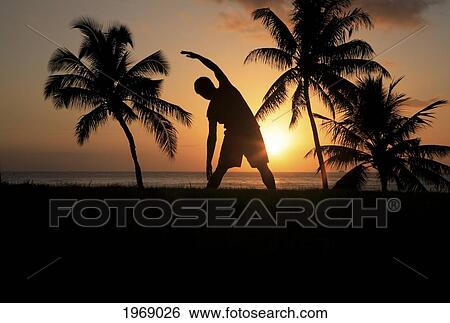 Stock Photograph - Hawaii, Oahu, Silhouette Of Man Stretching Near The Beach As The Golden Sunsets. Fotosearch