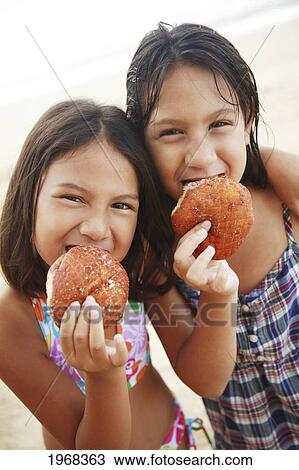 Stock Image - Hawaii, Oahu, Two Young Girls Enjoying Yummy Malasadas.. Fotosearch