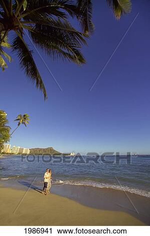 Stock Image - Hawaii, Oahu, Waikiki Beach, Couple Walking Down The Beach With Diamond Head In The Background.. Fotosearch