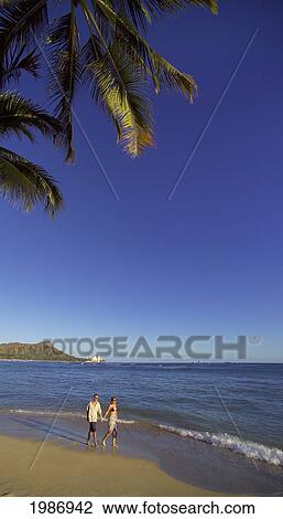 Stock Image - Hawaii, Oahu, Waikiki Beach, Couple Walking Down The Beach With Diamond Head In The Background.. Fotosearch