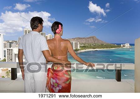 Stock Image - Hawaii, Oahu, Waikiki, Couple On Hotel Balcony Overlooking Waikiki Beach And Diamond Head, View From Behind.. Fotosearch