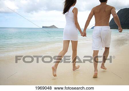 Stock Photo - Hawaii, Oahu, Waimanalo, Young Couple Holding Hands Running Together Along The Beach. Fotosearch