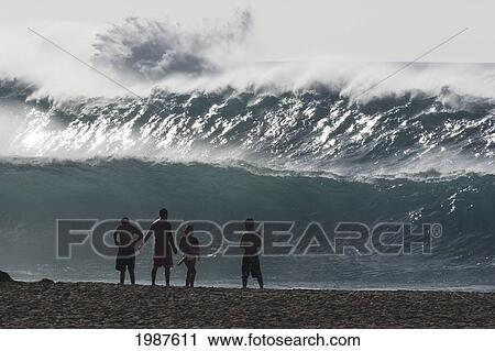 Stock Image - Hawaii, Oahu, Waimea Bay, Silhouette Of Group Of People Standing On The Beach At Watching Big Surf. Fotosearch
