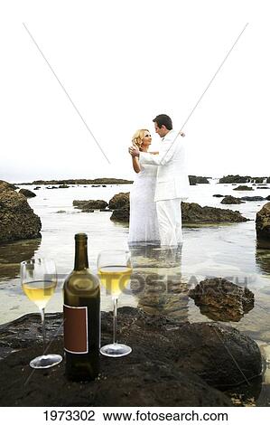 Stock Image - Hawaii, Oahu, Wedding Couple Kissing In The Tidepool With Wine Bottle And Two Glasses Left On A Rock In Foreground.. Fotosearch