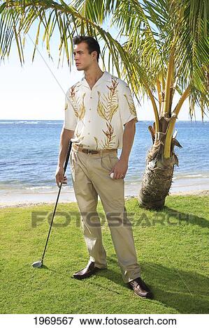 Stock Photo - Hawaii, Oahu, Well Dressed Male Standing With Golf Club And Golf Ball In Hand At A Beautiful Beachfront Golf Course Turf.. Fotosearch