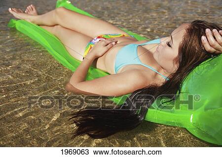 Stock Image - Hawaii, Oahu, Young Beautiful Female Relaxing On A Bright Beach Floater In The Water. Fotosearch