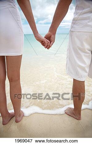 Hawaii, Oahu, Young Engaged Couple Facing The Beach Holding Hands, View From Behind View Large Photo Image Stock Photo - Hawaii, Oahu, Young Engaged Couple Facing The Beach Holding Hands, View From Behind. Fotosearch