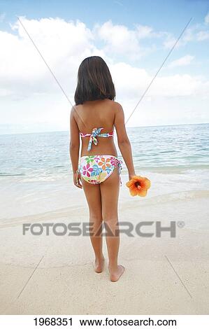Stock Image - Hawaii, Oahu, Young Girl Holding A Hibiscus Flower, View From Behind.. Fotosearch