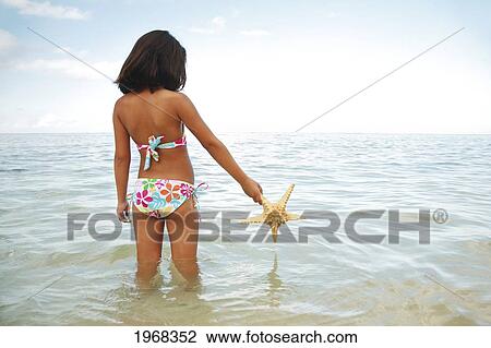 Stock Image - Hawaii, Oahu, Young Girl Holding A Starfish, View From Behind.. Fotosearch