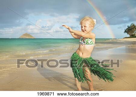 Stock Image - Hawaii, Oahu, Young Girl In A Hula Skirt Dancing On The Beach, Rainbow In Background.. Fotosearch