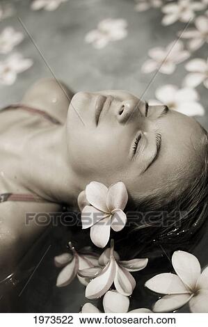 Stock Image - Hawaii, Oahu, Young Girl Resting In A Pool With Plumerias (Muted Colored Photo).. Fotosearch