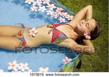 Stock Photograph - Hawaii, Oahu, Young Girl Resting In A Pool With Plumerias.. Fotosearch