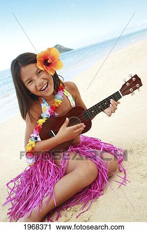 Stock Image - Hawaii, Oahu, Young Girl Smiling And Playing Ukulele On The Beach In A Hula Skirt.. Fotosearch