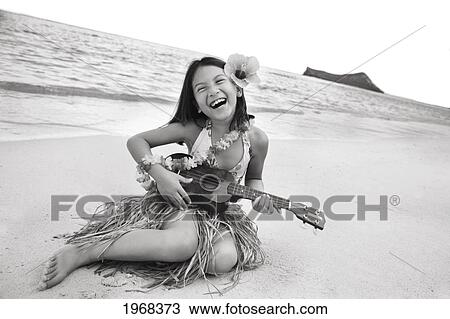Stock Image - Hawaii, Oahu, Young Girl Smiling And Playing Ukulele On The Beach In A Hula Skirt.. Fotosearch