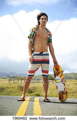 Stock Image - Hawaii, Oahu, Young Male Posing In Middle Of Roadway Holding A Skateboard.. Fotosearch