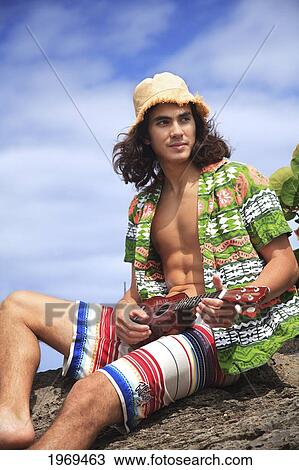 Stock Image - Hawaii, Oahu, Young Male With Vintage Aloha Shirt And Straw Hat Relaxing Holding A Ukulele.. Fotosearch