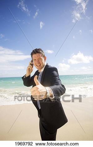 Stock Image - Hawaii, Oahu, Young Man At The Beach In Business Attire Giving 'thumbs-Up'.. Fotosearch