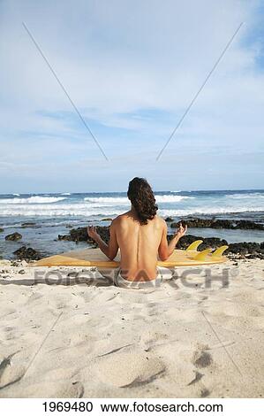Stock Image - Hawaii, Oahu, Young Man At The Beach Meditating With Surfboard.. Fotosearch