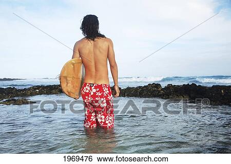 Stock Photograph - Hawaii, Oahu, Young Man In The Ocean Holding Surfboard. Fotosearch
