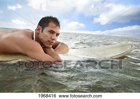 Stock Photograph - Hawaii, Oahu, Young Man Sitting On His Surfboard In The Water.. Fotosearch
