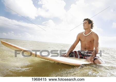 Stock Photography - Hawaii, Oahu, Young Man Sitting On His Surfboard At The Shoreline.. Fotosearch