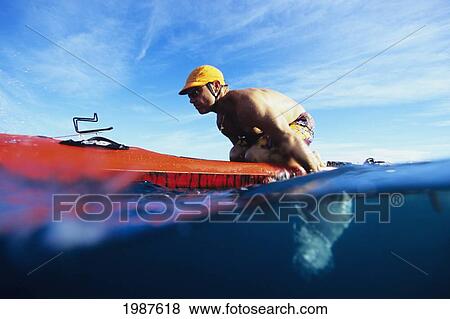 Stock Photo - Hawaii, Over/Under View Of Man Paddleboarding, Leaning Forward On Red Board.. Fotosearch
