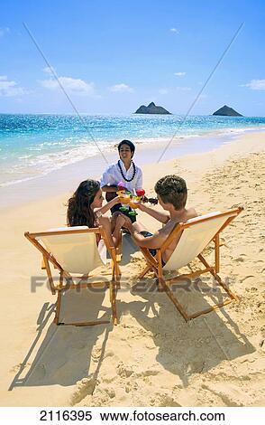 Stock Photography - Hawaii, polynesian man plays the ukulele for a young couple on the beach. Fotosearch
