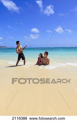 Hawaii, polynesian man plays ukulele for a young couple in the ocean. View Large Photo Image Stock Photo - Hawaii, polynesian man plays ukulele for a young couple in the ocean.. Fotosearch
