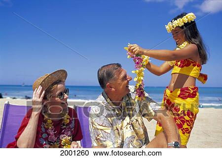 Stock Image - Hawaii, Senior Tourist Couple Receive Leis From Girl, Beach Scene Blue Sky D1468. Fotosearch
