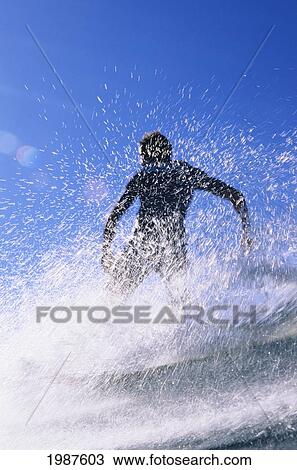Stock Image - Hawaii, Silhouette Of Man Riding Wave On Longboard Amid Ocean Spray. No Model Release. Fotosearch