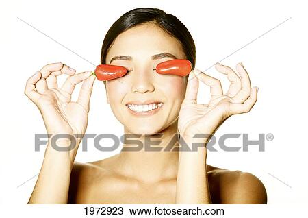 Stock Image - Hawaii, Studio Headshot Of A Beautiful Girl Holding Peppers Over Her Eyes.. Fotosearch