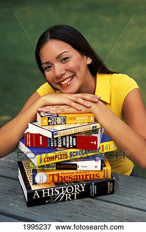 Stock Photo - Hawaii, Teen Girl In Yellow Resting Hands/Chin On Stack Of Books On Table.. Fotosearch