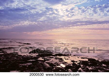 Stock Image - Hawaii, Tranquil Ocean Scene At Sunset, Soft Pink Hue, Rocky Shoreline With Small Waves. Fotosearch
