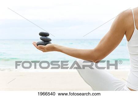 Stock Image - Hawaii, Woman Holding Stack Of Stones In Hands, Ocean In Background.. Fotosearch