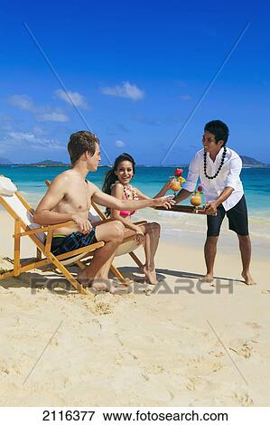 Stock Photo - Hawaii, Young couple on the beach in lounge chairs with tropical drinks.. Fotosearch
