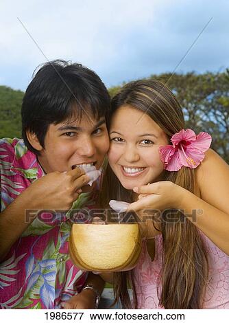 Stock Photo - Hawaii, Young Local Man And Woman Eating Poi With Fingers Out Of Wooden Bowl.. Fotosearch