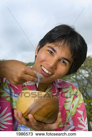Stock Image - Hawaii, Young Man Eating Poi With Fingers Out Of Wooden Bowl.. Fotosearch