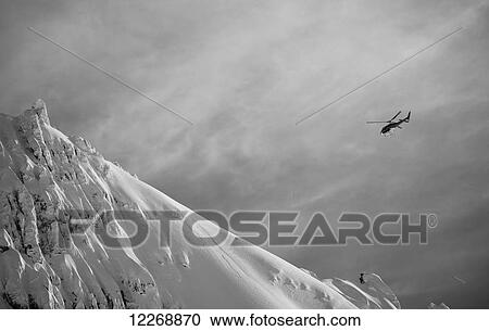 Stock Image - Helicopter flies through cloudy skies to a snowy mountain peak; New Zealand. Fotosearch