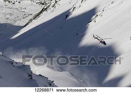 Stock Image - Helicopter flies through snowy mountains; New Zealand. Fotosearch