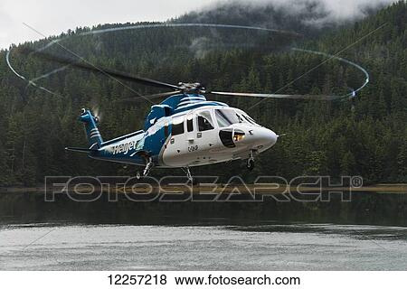 Stock Photo - Helicopter hovering over water while taking off; Queen Charlotte Islands, British Columbia, Canada. Fotosearch