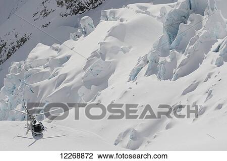 Stock Image - Helicopter landing on snowy mountain ridge; New Zealand. Fotosearch