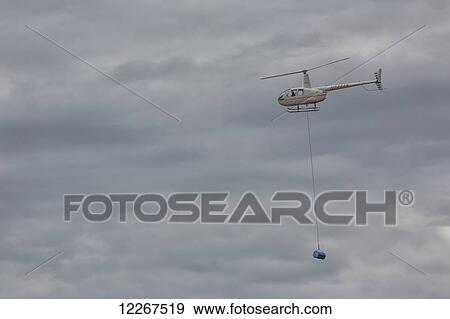 Stock Photo - Helicopter shuttling fuel barrels to a roadless community; Old Crow, Yukon, Canada. Fotosearch