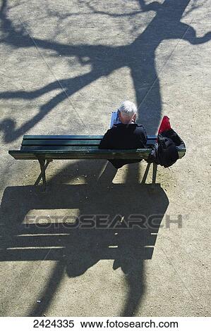 Stock Photography - High angle view of a man sitting on a park bench and the shadow of a tree cast over him; Paris, France. Fotosearch