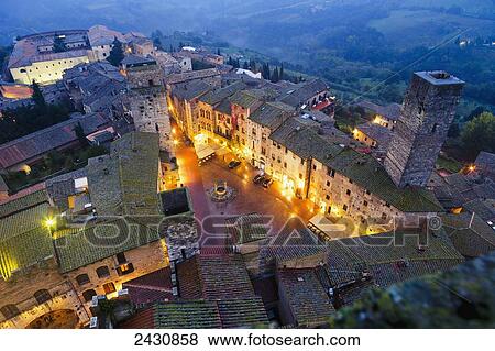 Stock Photo - High angle view of the town with lights illuminating the buildings at dusk; San Gimignano, Tuscany, Italy. Fotosearch