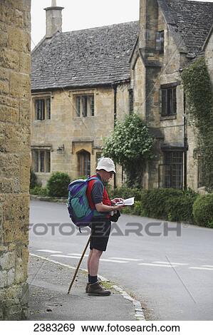 Hiker checking directions in Stanton village with honey coloured Cotswold limestone buildings in the background; Gloucestershire, England View Large Photo Image Stock Photo - Hiker checking directions in Stanton village with honey coloured Cotswold limestone buildings in the background; Gloucestershire, England. Fotosearch